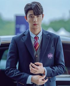 a young man in a suit and tie standing next to a car with his hand on his pocket