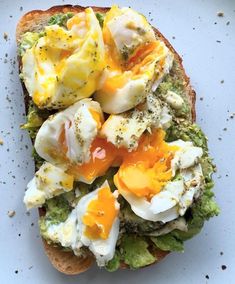 an open face sandwich with eggs and broccoli on it, sitting on a white plate