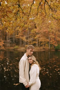 a pregnant couple standing next to each other in front of a lake