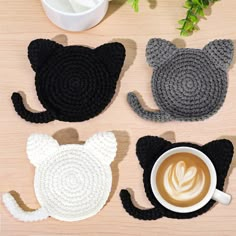 four crocheted cat coasters sitting on top of a wooden table next to a cup of coffee