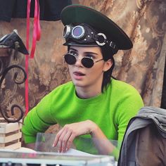 a woman wearing a green shirt and black hat sitting at a table with a laptop