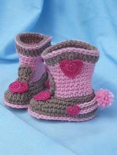 crocheted booties with hearts on them sitting on a blue cloth covered background