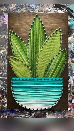 a painting of a green plant in a blue vase on a wooden board with paint splatters