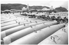 black and white photograph of large pipes with planes in the background at an air port