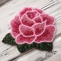 a pink rose with green leaves on a wooden surface