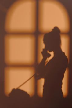 the silhouette of a woman talking on her cell phone in front of an open window