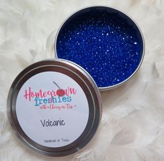 two tins of blue glitter sitting next to each other on a white background with feathers