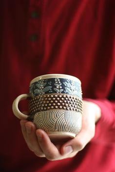 a person is holding two cups in their hands, one with designs on it and the other without