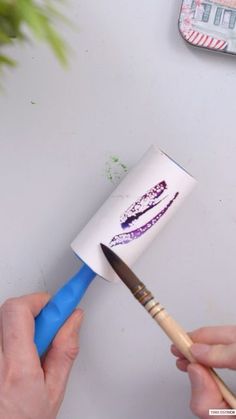 a person holding a paint brush near a cup with lipstick drawn on it and another hand holding a pencil