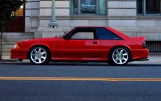 a red car is parked on the side of the road in front of a building