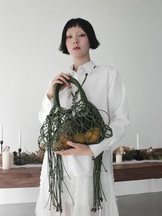 a woman holding a green bag with oranges in it's hands and wearing a white shirt