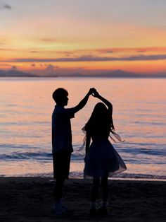 two people holding hands on the beach at sunset