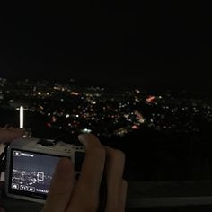 a person taking a photo with their cell phone at night in front of the city lights