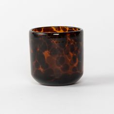 a brown and black glass vase sitting on top of a white table next to a wall