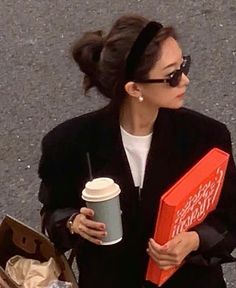 a woman walking down the street holding a coffee cup and a paper bag with a donut in it