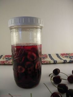 a jar filled with cherries sitting on top of a table next to a cloth