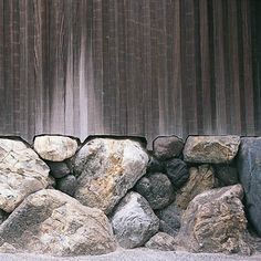 a cat sitting on top of a pile of rocks next to a wooden fence and wall