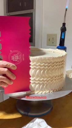 a person is holding up a cake with pink frosting on the top and bottom