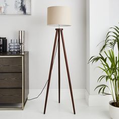 a wooden tripod floor lamp next to a potted plant in a white room