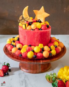 a red cake with fruit and stars on top is sitting on a wooden platter