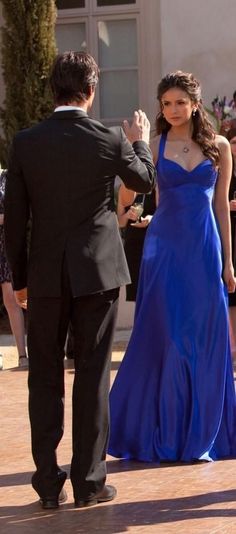 a woman in a blue dress standing next to a man in a tuxedo