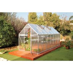 a small greenhouse sitting on top of a wooden platform next to a lush green field