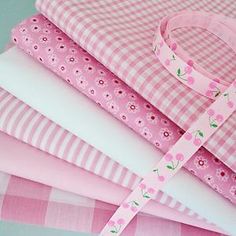 a stack of pink and white fabrics with flowers on them, all lined up together