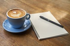 a cup of coffee on a saucer next to a notepad with a heart drawn in it