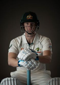 a man sitting on top of a wooden chair wearing a helmet and holding a cricket bat