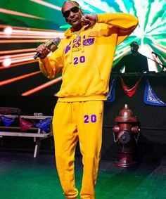 a man in a yellow sweatshirt and sweatpants stands on stage with fireworks behind him