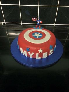 a birthday cake with captain america frosting and stars on the top, sitting in front of a tiled wall