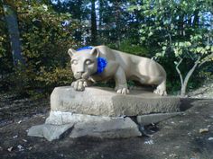 a statue of a cougat sitting on top of a stone slab in front of trees