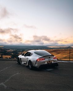 a silver sports car parked on the side of a road at sunset with clouds in the background