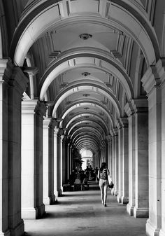 a black and white photo of people walking down a long hallway lined with arches,