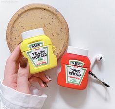 a hand holding a bottle of mustard next to a container of ketchup on a white surface