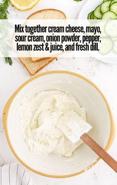 a white bowl filled with cream cheese next to sliced cucumbers and lemon slices