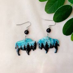 a pair of earrings with an image of a bison and trees on it, sitting next to some leaves