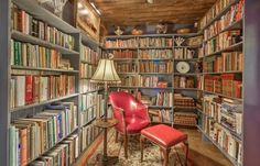 a room filled with lots of books next to a red chair and two lamps on either side of the bookcases