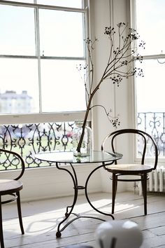 two chairs sitting in front of a glass table with flowers on it next to a window