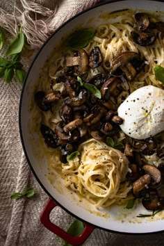 a pan filled with pasta and mushrooms on top of a table next to a cloth