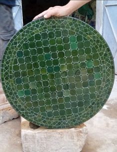 a green plate sitting on top of a block of cement next to a person's hand