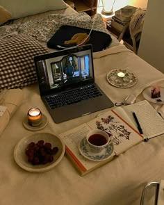 an open laptop computer sitting on top of a bed next to a bowl of grapes