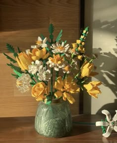 a green vase filled with yellow and white flowers