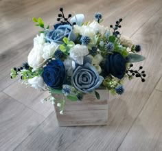 a blue and white flower arrangement in a wooden box on the floor with wood planks