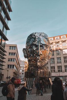 people are standing around in front of a building with a giant head on it's face