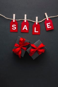 red tags with the word sale hanging from clothes pins and tied to strings on a black background