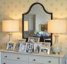 a white dresser topped with two lamps next to a mirror and pictures on top of it