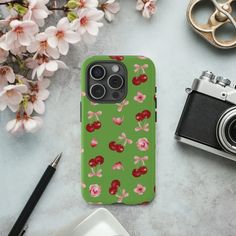 a green phone case with cherries on it next to a camera and some flowers