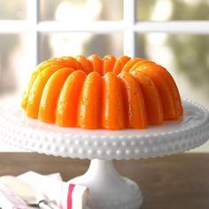 an orange bundt cake sitting on top of a white platter next to a window