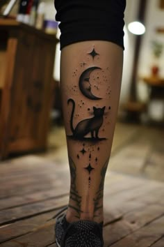 a woman's leg with a cat and moon tattoo on it, sitting on a wooden floor